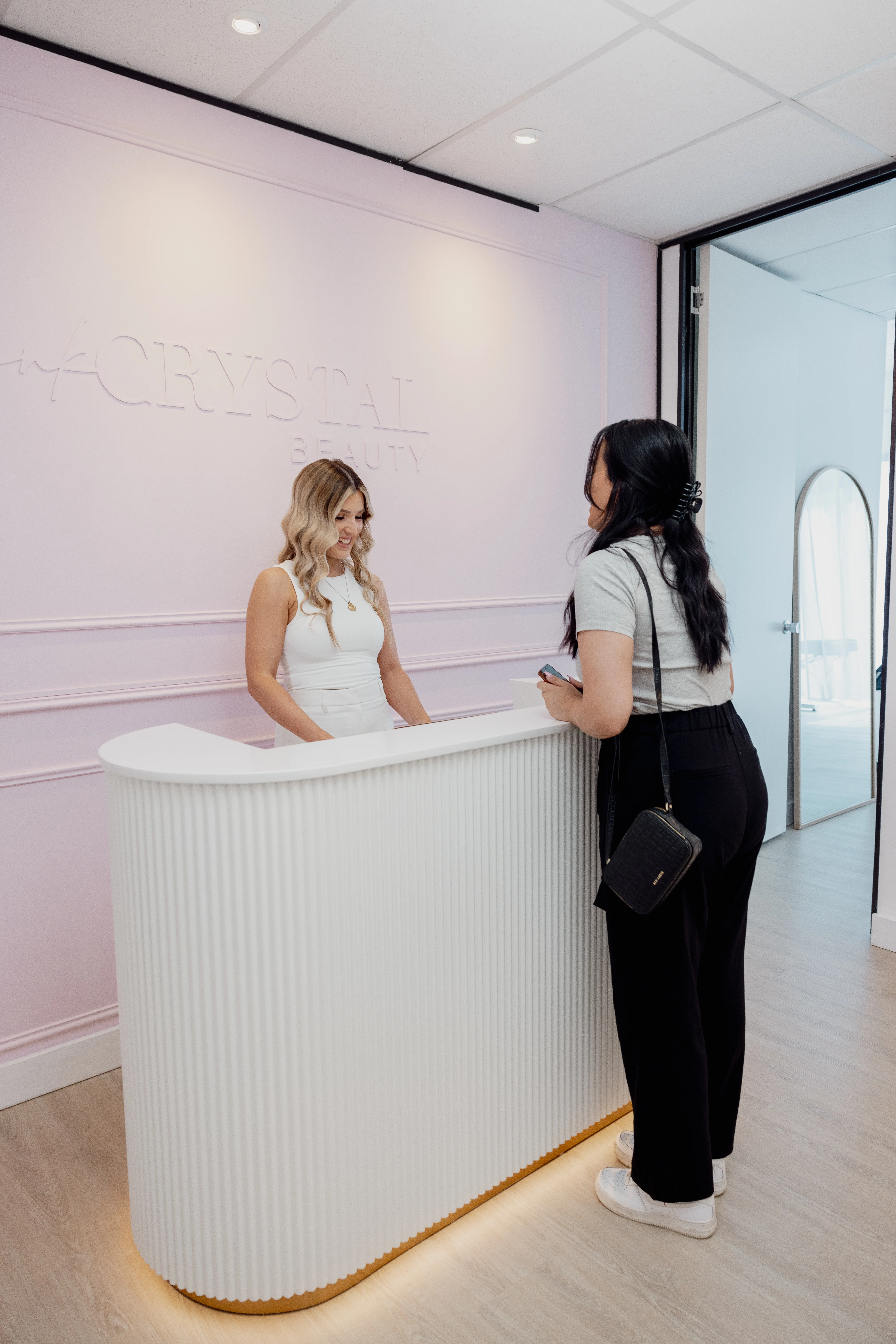 The fluted white reception desk viewed from the room, a practitioner in white behind it, with an archway and corridor visible beyond