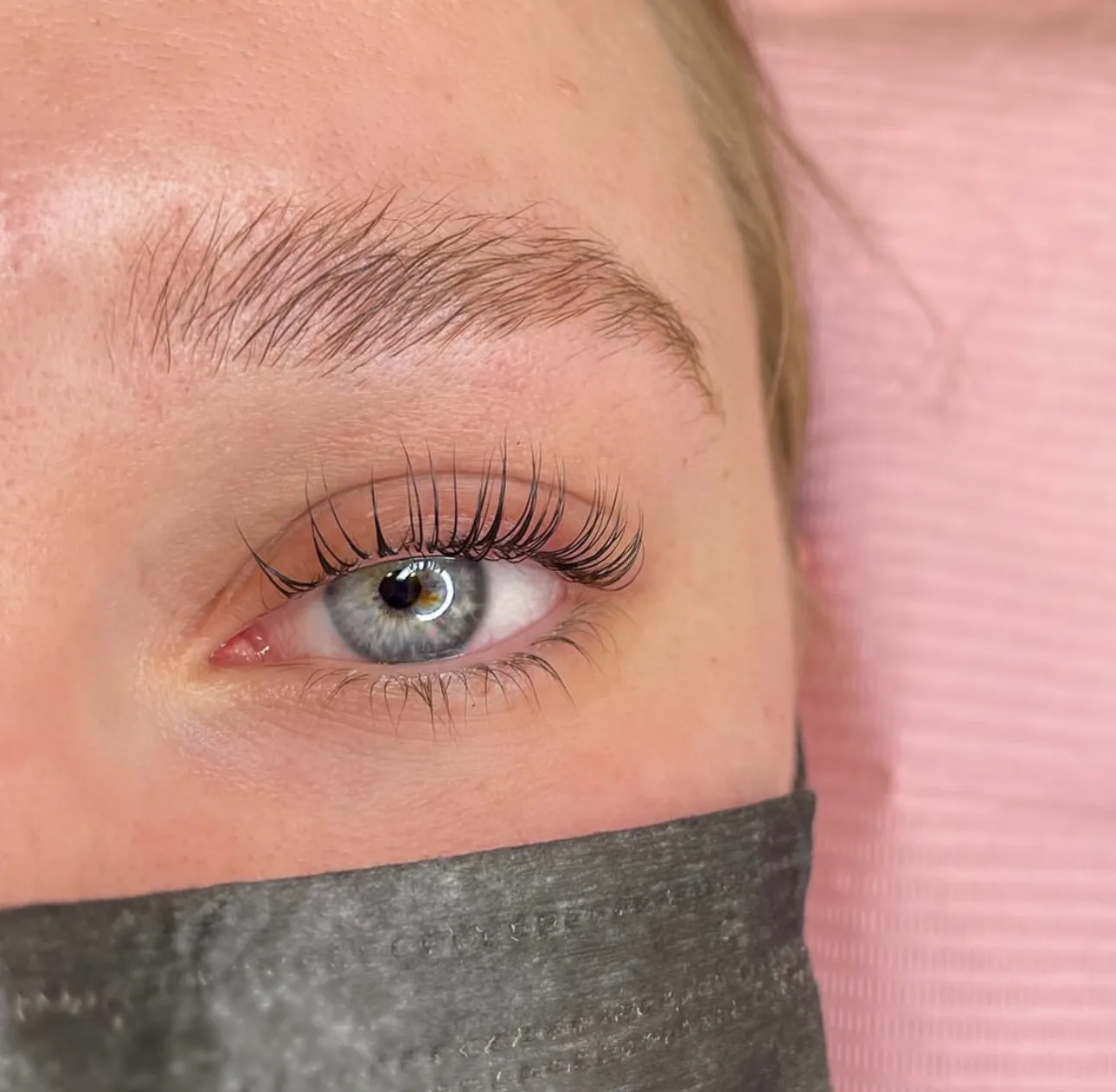 Client on a pink treatment bed with lifted and tinted natural lashes on an open blue eye